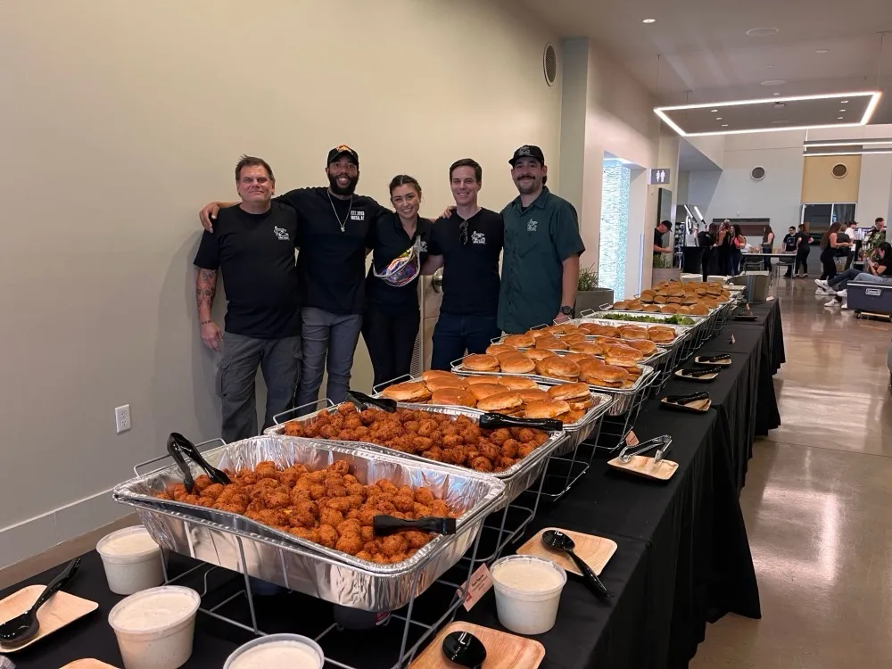 Five team members behind a long catering table of sandwiches and bites