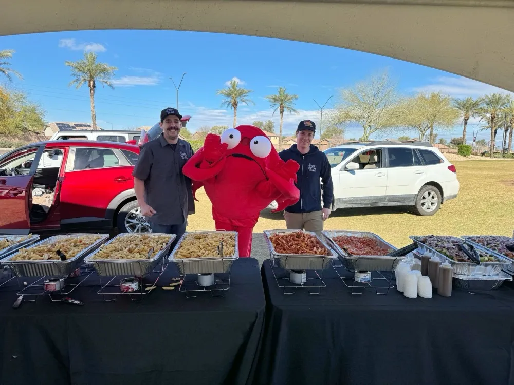 The Angry Crab mascot with two team members at an outdoor catering table