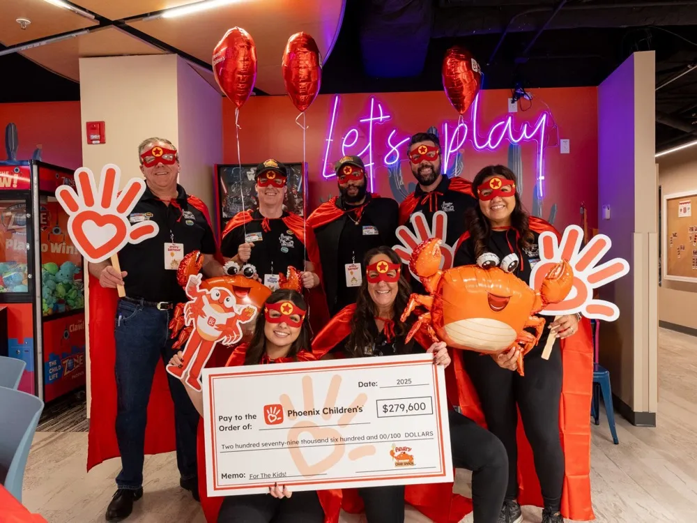 The team in red capes and masks holding a $279,600 cheque for Phoenix Children’s
