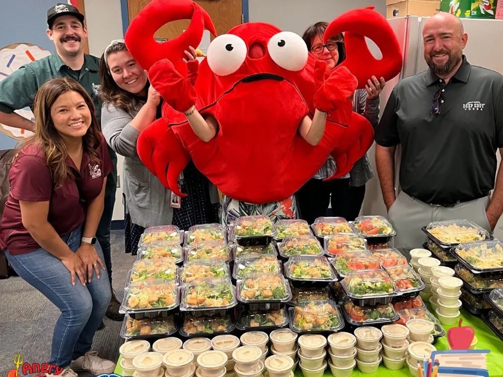The Angry Crab mascot and team behind a table of boxed meals for teachers