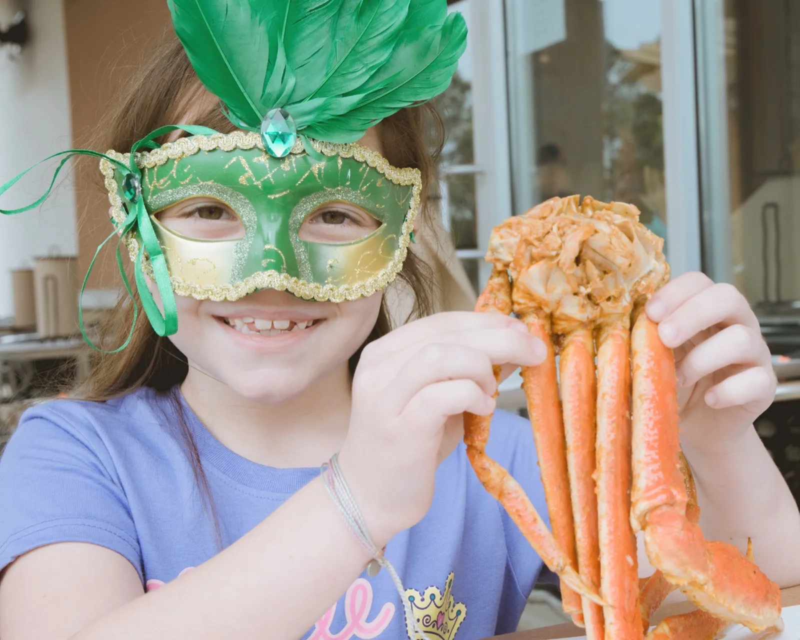 A smiling child in a green mask holding up crab legs